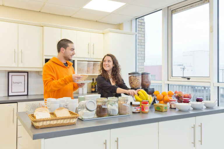 Two people in the kitchen with food at Canbe Hostels - Garden Lane