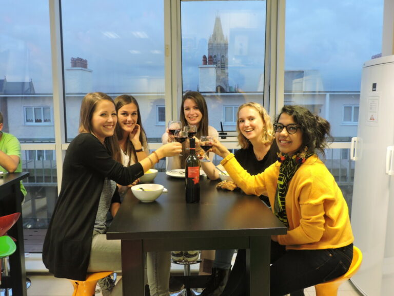 Five girls with drinks celebrating cheers with window in background at Canbe Hostels - Garden Lane