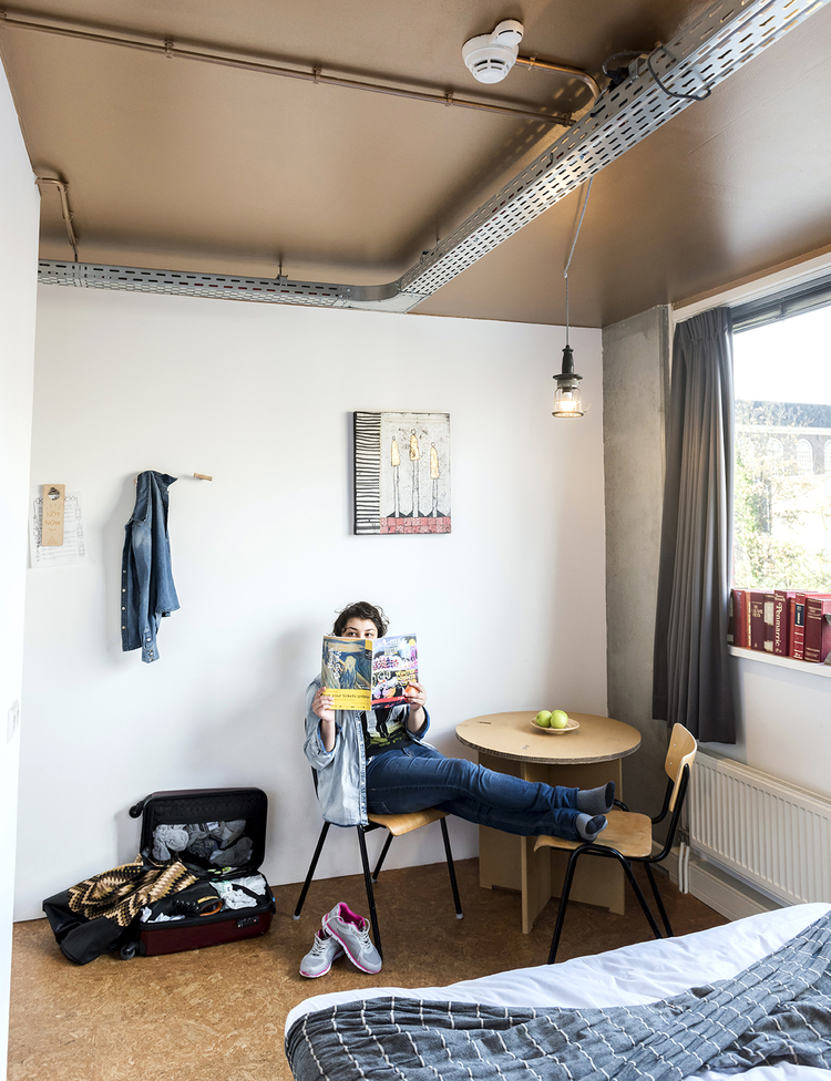 Room at Ecomama hostel in Amsterdam with a guest reading at a table 